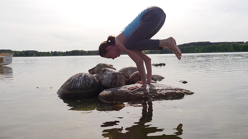 woman in crow pose on a stone in water