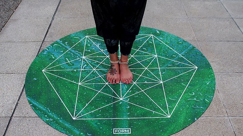 feet standing on a round yoga mat that looks like one of the chakra symbols