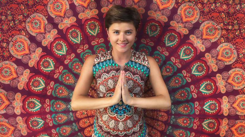 woman in a greeting Namasté pose in front of a mandala fabric 